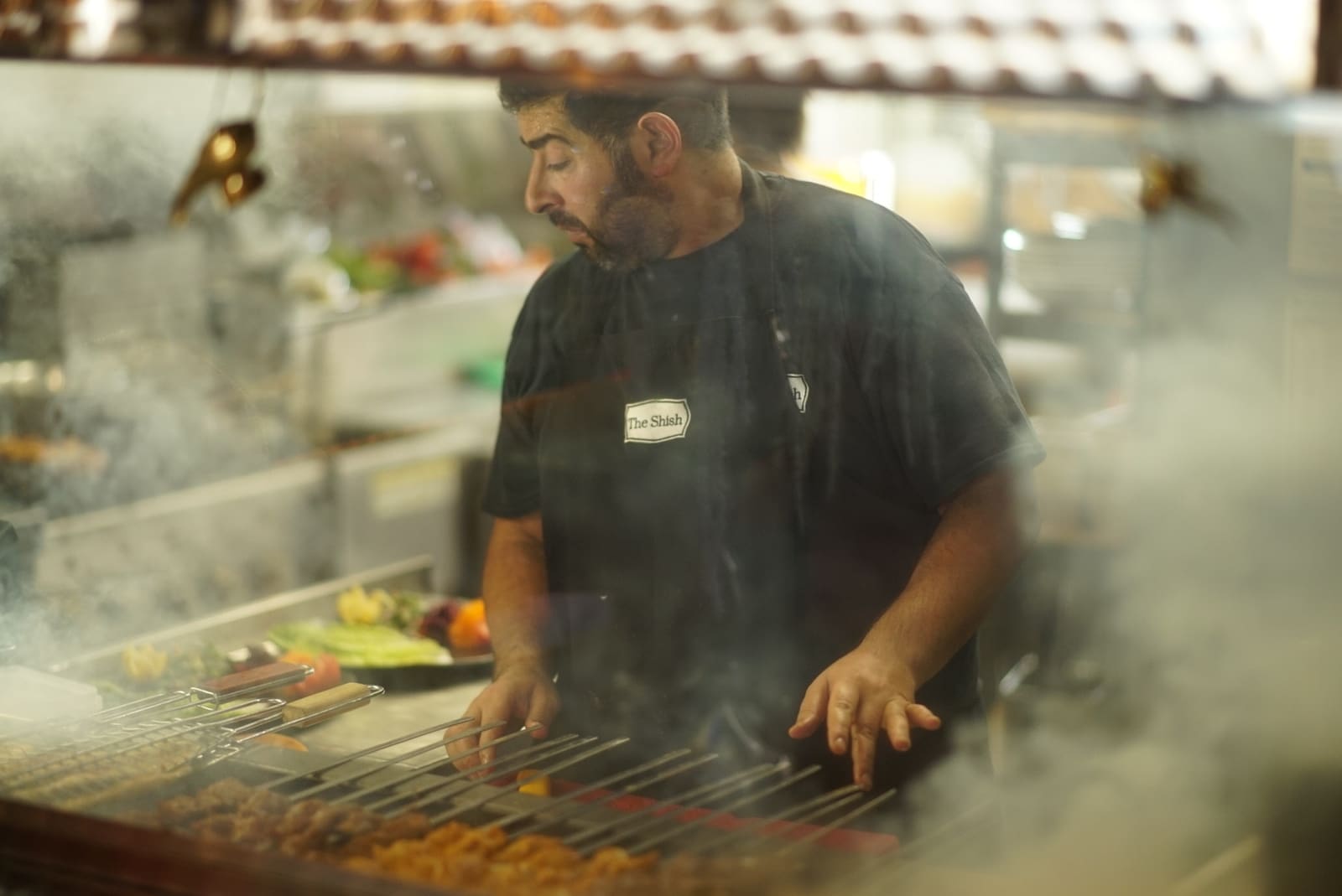 A cook turning skewers over the charcoal grill at The Shish